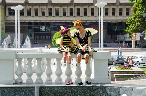 Kharkiv, Ukraine - June 18, 2016: Mother and daughter dreessed in costumes of bees are drying their feet after washing them in the fountain. Costumed bike ride \