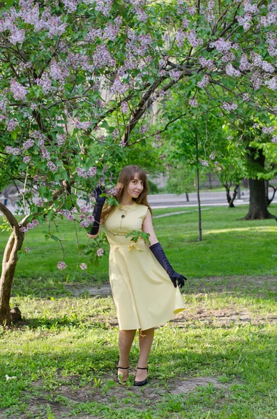Beautiful blond girl in a lemon-yellow dress posing in lilac
