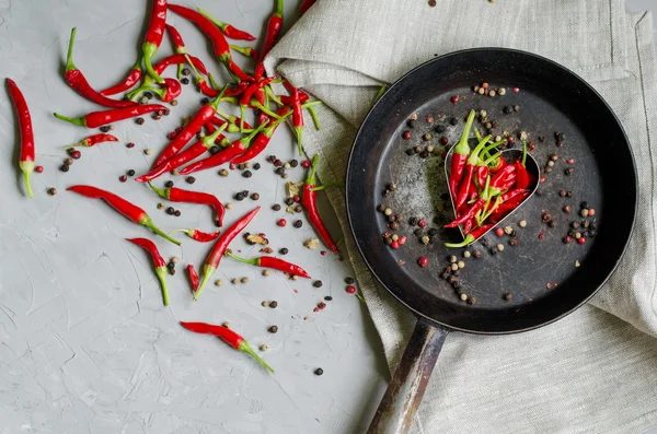 Little chilly peppers in a heart shape on an iron frying pan on gray background, concept of hot love and passion