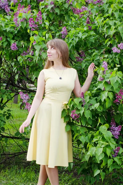 Beautiful blond girl in a lemon-yellow dress posing in lilac
