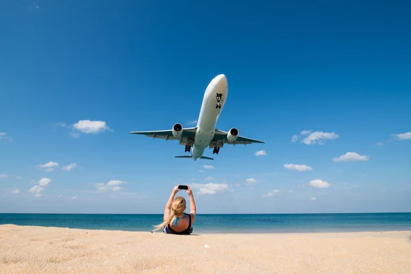 Woman shoot a photo of landing plane on beach