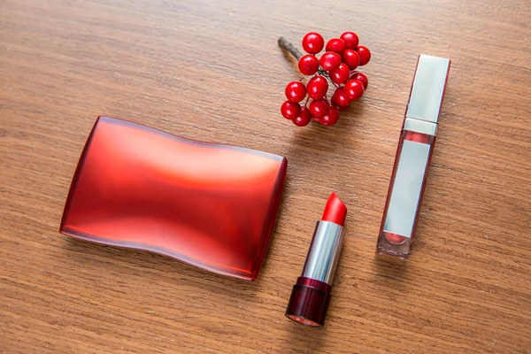 Red lipstick, lip gloss and powder box on a wooden background