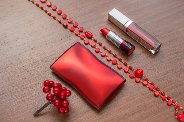 Red lipstick, lip gloss and powder box on a wooden background