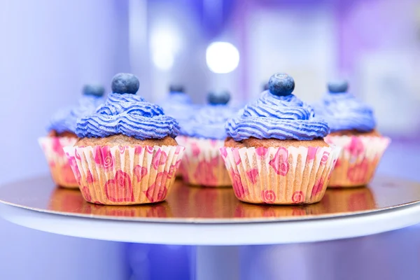Blueberry muffin on a stand. Party decorations food. Cupcakes with berries and cream. Purple color cakes.
