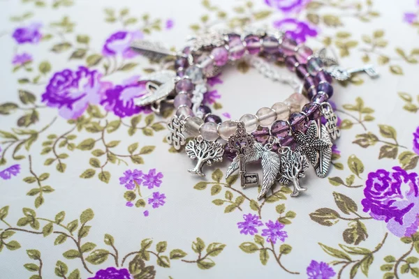 Silver bracelet with natural stones, shaped beads and crystals on a purple textile background