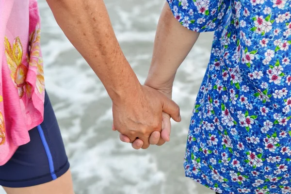 Old couple holds hand along the beach