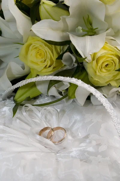 Wedding bouquet of lilies and roses, gold wedding rings on a cushion