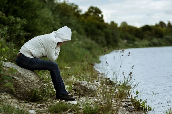 Lonely woman sitting back in jacket with a hood on the banks of river