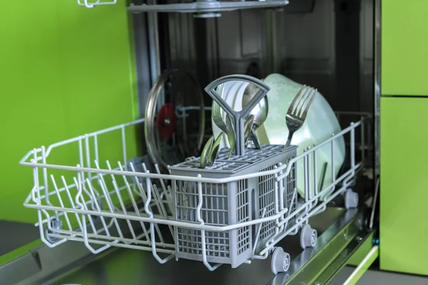 Clean dishes in the dishwasher on background of green furniture