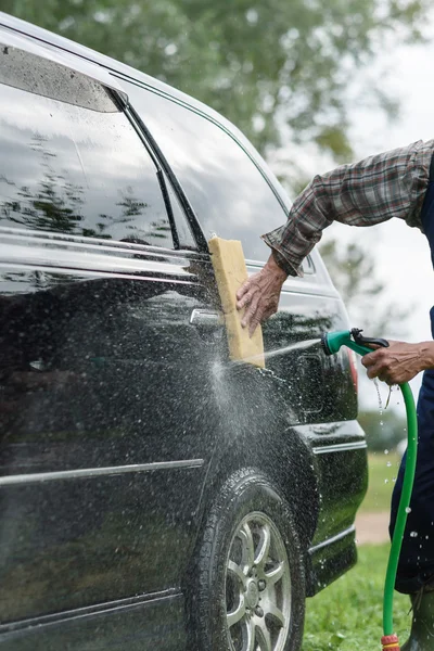 Man washes his car on background of green garden