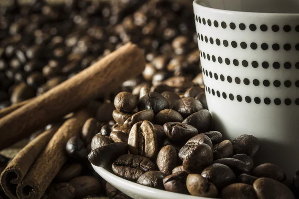 White Coffee mug with polka dots with coffee beans and cinnamon sticks.