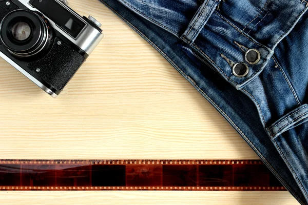 Camera, film and denim pants lying on the wooden background. Youth photo equipment Photographer