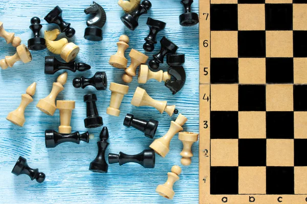 Old cropped chessboard with black and white figures on blue wooden background. Top view. Flat lay.
