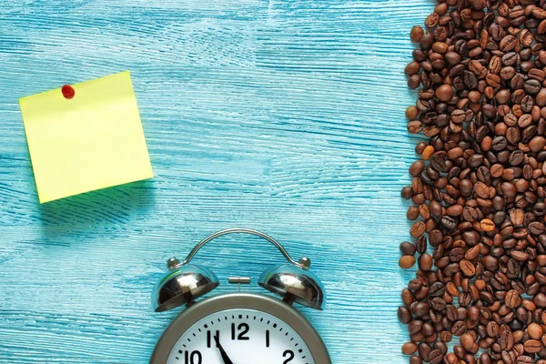 Coffee beans, old alarm clock with bells and a paper sticker notes on a blue wooden background. Top view. Flat lay