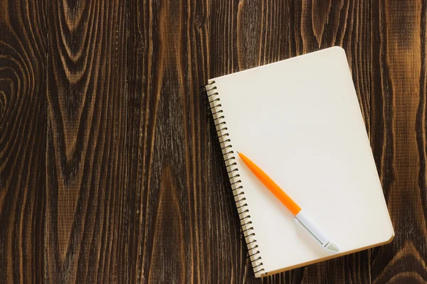 Single simple empty white notebook with a blank for drawing or writing and white plastic pen are on a Desktop from wooden plank. Top view. Mock up. Flat lay