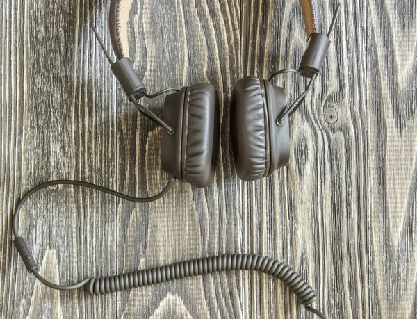 Headphones with cord lying on wooden background. Top view