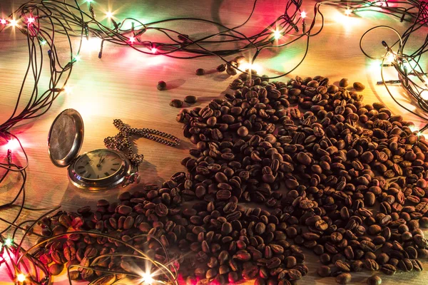 New year or chrismass background. Pocket watch, and spilled coffee beans on a wooden desk surrounded by holiday garland