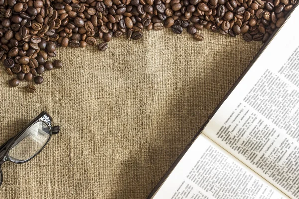 Background of roasted coffee beans scattered on the canvas of burlap, glasses and open book
