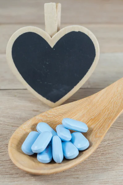 Blue pills in wooden spoon with blank heart shape blackboard