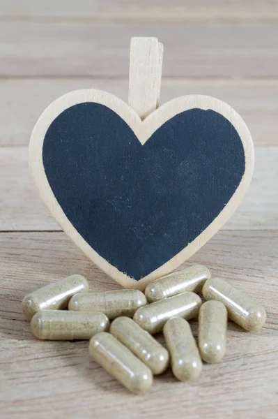 Capsule pills with blank heart shape blackboard on wood backgro