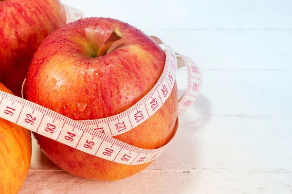 Fresh apples with measure tape on white wood background