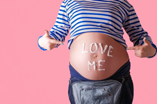 Pregnant woman writing love me word on her belly. Trendy Pink background.