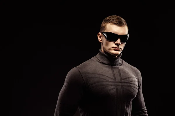 Combat muscled action hero man wearing brown sweater and sunglasses. Studio shot.