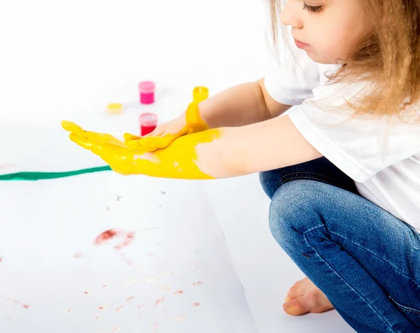 Pretty child girl smears yellow paint on hands