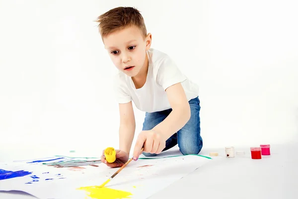 Child with paintbrush. 9 year Boy, modern hair style, white shirt, blue jeans is drawing paint brush isolated. Studio.