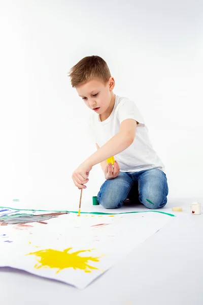 Child with paintbrush. 9 year Boy, modern hair style, white shirt, blue jeans is drawing paint brush isolated. Studio.