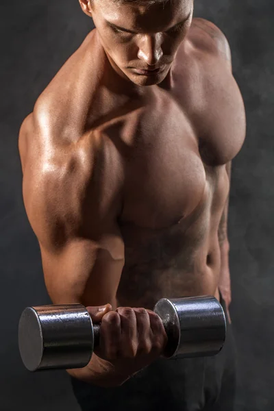 Closeup of a handsome power athletic man bodybuilder doing exercises with dumbbell. Fitness muscular body on dark background. Perfect male. Awesome bodybuilder, tattoo, posing.