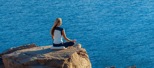Woman Sitting in Lotus Position on Rock Above the Sea and Meditating. Yoga Outdoor. copyspase
