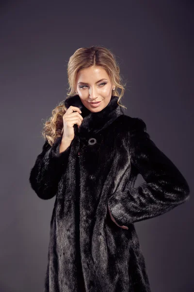 Fashion seductive blond hair lady in an elegant fur coat and black underwear on a dark background. Retouched.