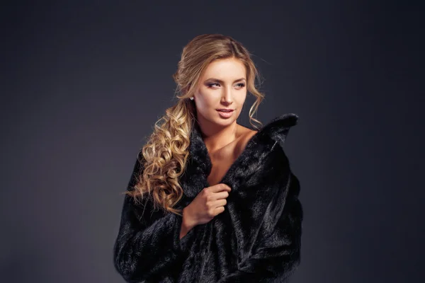 Fashion seductive blond hair lady in an elegant fur coat and black underwear on a dark background. Retouched.