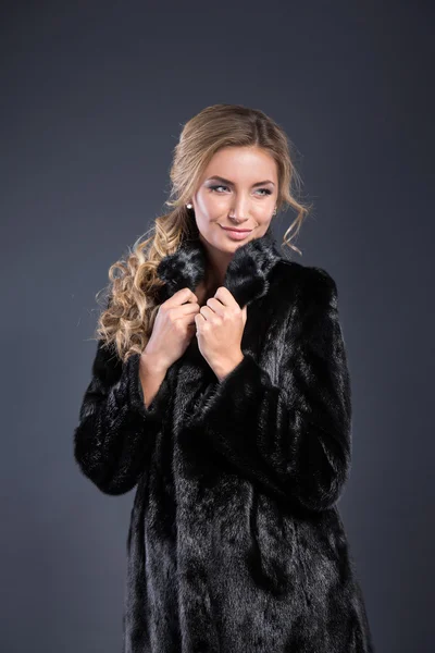 Fashion seductive blond hair lady in an elegant fur coat and black underwear on a dark background. Retouched.