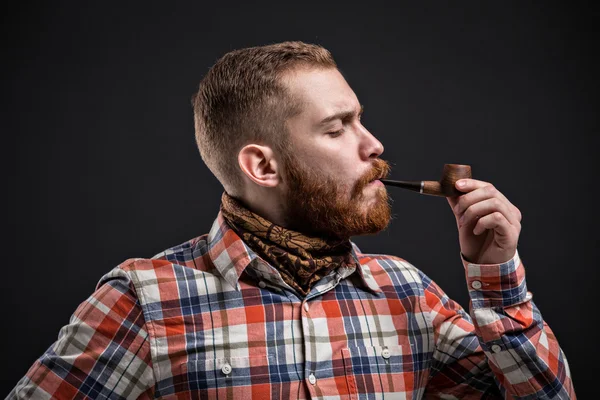 Portrait of bearded man smoking pipe with squinted eye