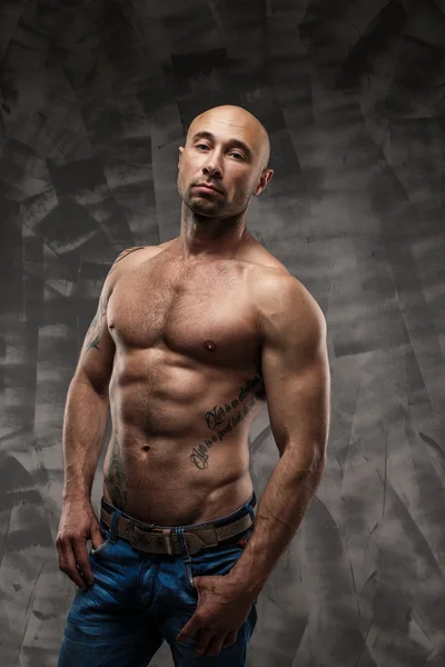 Shirtless muscled fitness man. Cool looking. Tough guy. Brown eyes. Bald. Tanned skin. Studio shot on grey abstract background.