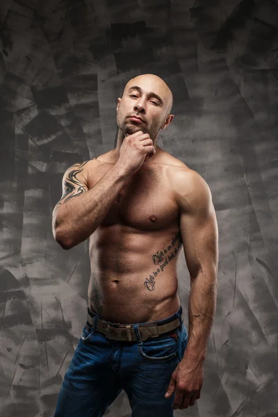 Shirtless muscled fitness man. Cool looking. Tough guy. Brown eyes. Bald. Tanned skin. Studio shot on grey abstract background.