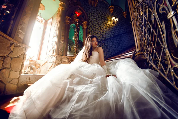 Young beautiful luxurious woman wearing wedding dress sitting on stair steps in semi-darkness.