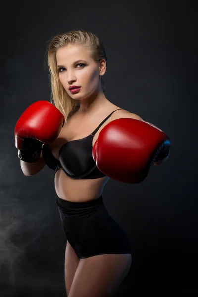 Beautiful woman with the red gloves is boxing on black background