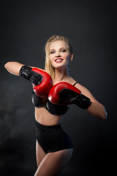 Beautiful woman with the red gloves is boxing on black background