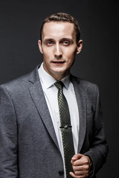 Serious business man brown hair with expressive face wearing grey suit and tie. Isolated on dark background.