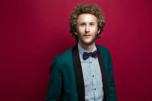 Bearded stylish man with curly hair wearing bow-tie, green jacket. Red background. Isolated