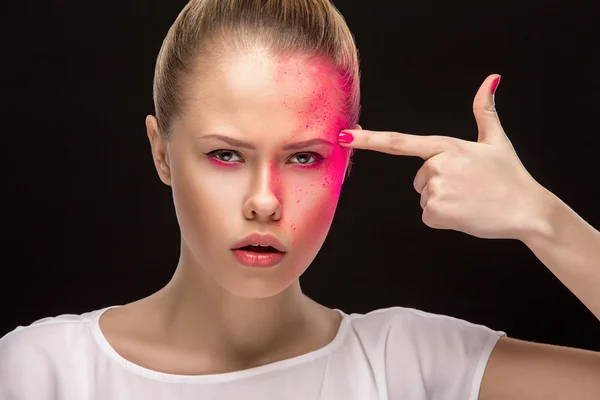 Concept of a portrait of young blond girl with a lot of pain of suicide on her face, pink make-up, purple eyeshadows looking at you with hand pistol on black background. Social theme.