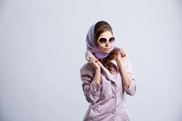 Young fashion woman posing in studio wearing pink coat and white sunglasses.