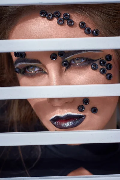 Fashion portrait with dark creative makeup, black lips,  behind bars