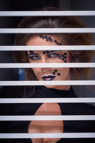 Fashion portrait with creative makeup, dark lined eyes,  behind bars