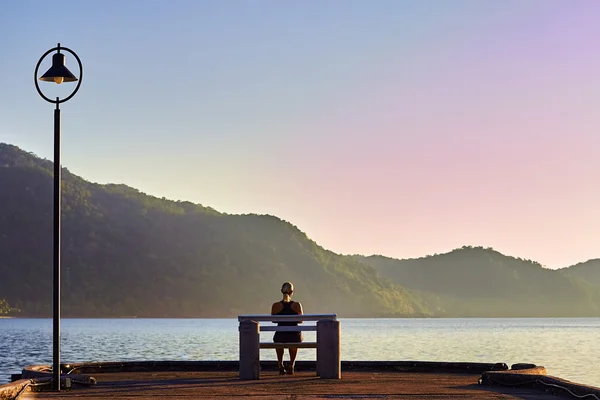 Woman sitting on bench. Sunrise near ocean. Morning meditation.