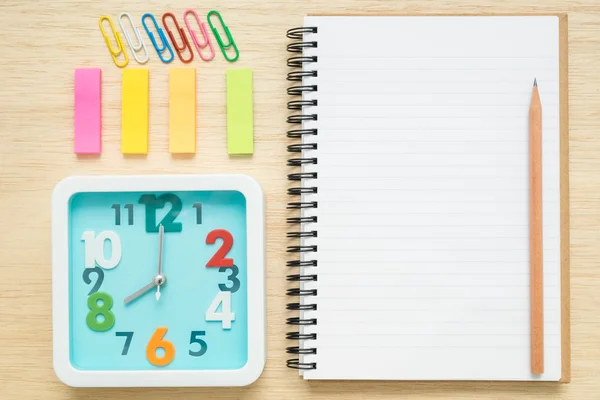 Top view notebook, clock, paper clips on wooden desk