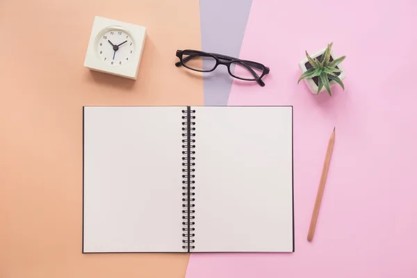 Top view of notebook with pen, eyeglasses, clock, plant on paste